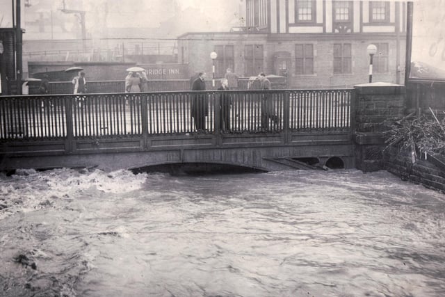 Passers-by casting some anxious looks as they cross Heeley Bridge and see that the water was getting dangerously near the top of the arch on July 2, 1958