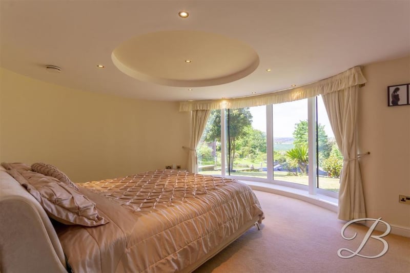 The main bedroom with a panoramic, curved window looking out on to the front of the property. There are also patio doors leading outside.