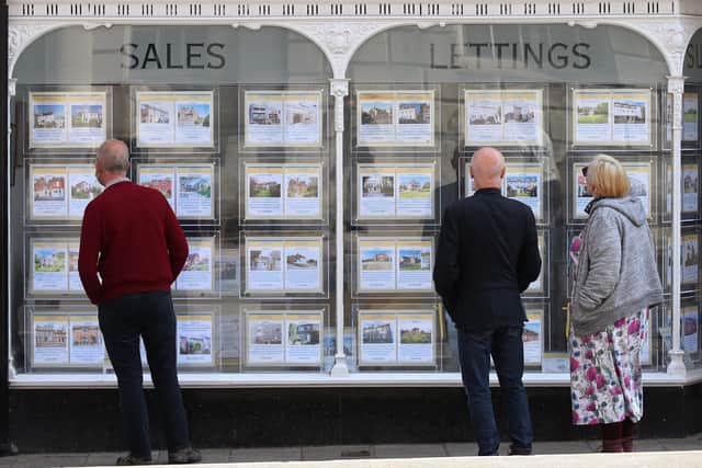 People looking at house price signs displayed in the window of an estate agents.