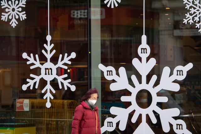 A woman wearing a face mask passes snowflake Christmas decorations in a store window - PA