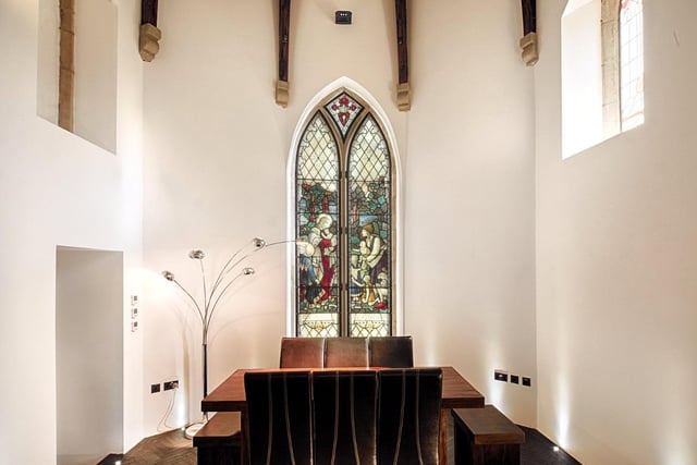 Steps from the main living area lead up to the dining room, which is set in the original alter with a stained glass window as its backdrop and wooden beams overhead.