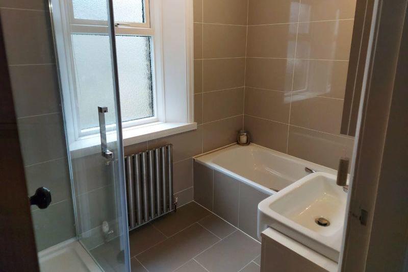With modern white three-piece suite comprising hand wash basin in vanity unit, fully tiled shower cubicle with overhead and handheld shower units and a panelled bath.