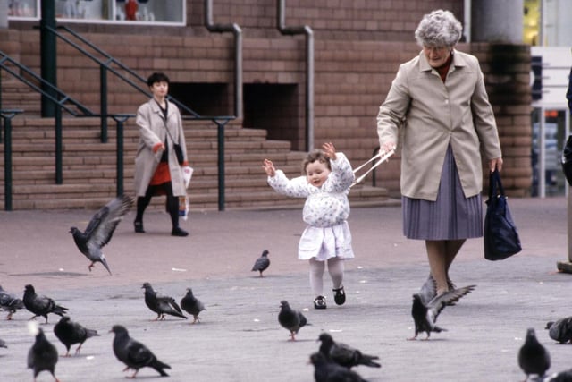 Granny holds onto a toddler's harness as she chats to the pigeons in Glasgow, August 1990.