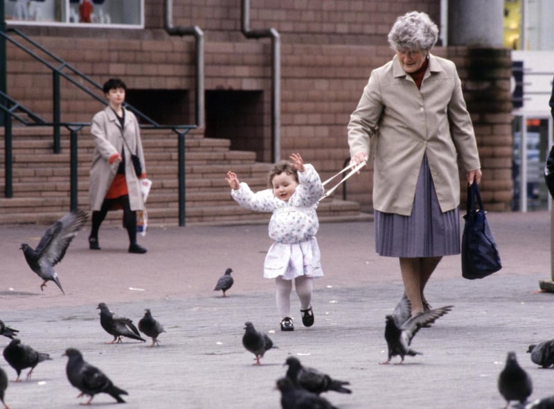 Granny holds onto a toddler's harness as she chats to the pigeons in Glasgow, August 1990.