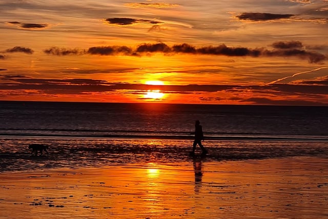 A lone walker enjoys the glow at the seaside.