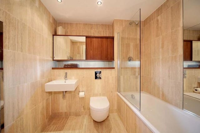The contemporary bathroom has a white suite with a shower over the bath, a heated chrome towel radiator and a wall mounted vanity cabinet with integrated shaver point and lighting.