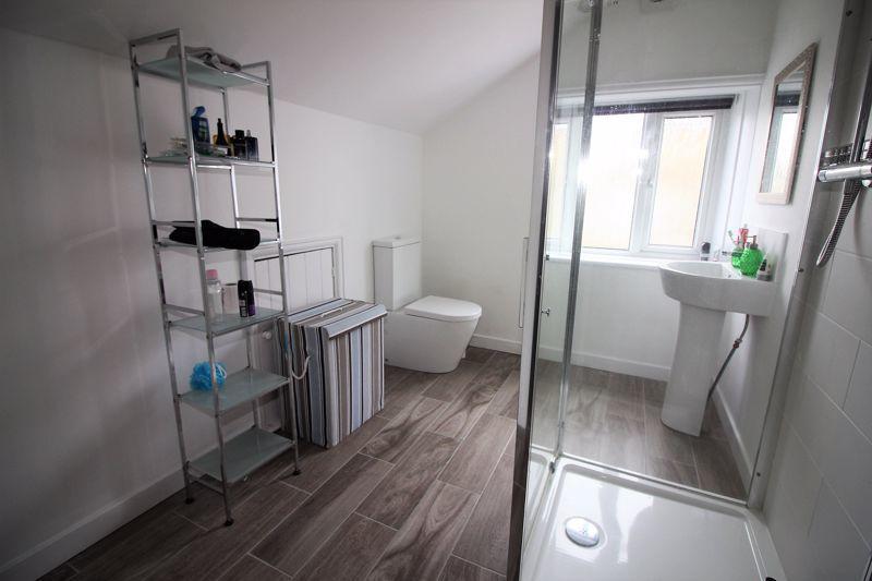 With modern white three-piece suite comprising pedestal wash basin, low-flush WC and fully tiled shower cubicle with overhead and handheld shower units.