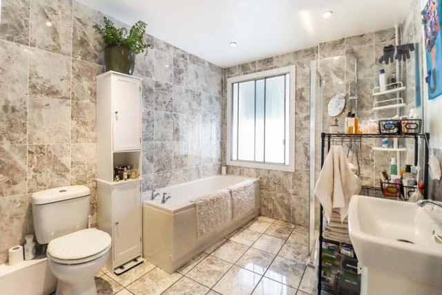 The spacious modern bathroom benefits from WC, wash hand basin set on vanity unit, bath and shower cubicle with power shower, modern tiling to floor/walls, and down lighting to ceiling.