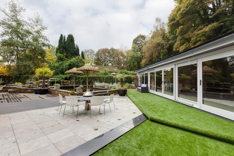 To the side, there are multiple seating areas including a stone flagged terrace with a timber decking area and an additional composite decking area with exterior lighting.