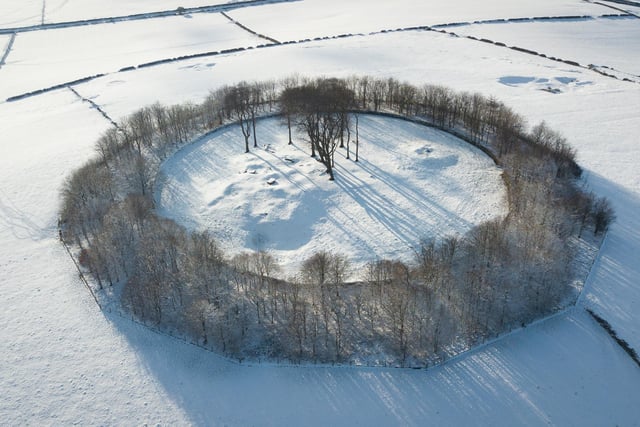 A snowy landscape frames Minninglow, a neolithic tomb and round barrow encircled with a ring of beech trees, near Parwich in the Derbyshire Peak District.