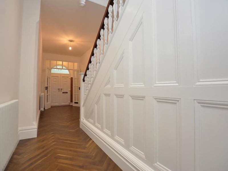 A welcoming hall features a high ceiling, new parquet flooring, LED spotlights, two feature column radiators and understairs storage cupboards. A wide, traditional staircase leads to the first-floor landing.