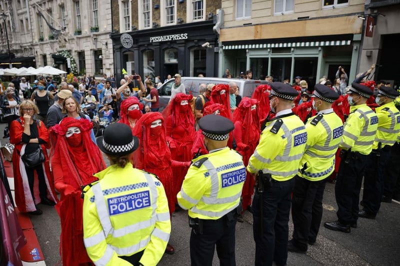 Members of the Red Rebel Brigade - an international performance artivist troupe - face a cordon of police officers as they join climate activists from the Extinction Rebellion group in central London (Photo by TOLGA AKMEN/AFP via Getty Images)
