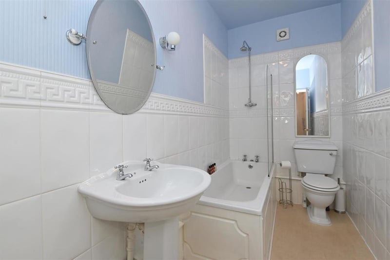 The ground-floor bathroom has a laminate floor and is tiled to half-height with patterned blue wallpaper above. A high-quality ceramic WC and pedestal sink complement the bath, which has a rainforest shower over and glass shower screen. There is a ceiling light, two wall lights and extractor fan.