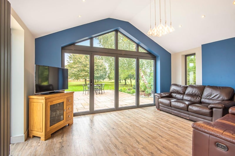 The spacious living room features laminate flooring, two ladder radiators, a high ceiling, inset ceiling lights, a window and bi-fold doors to the garden