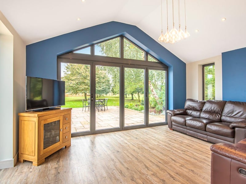 The spacious living room features laminate flooring, two ladder radiators, a high ceiling, inset ceiling lights, a window and bi-fold doors to the garden