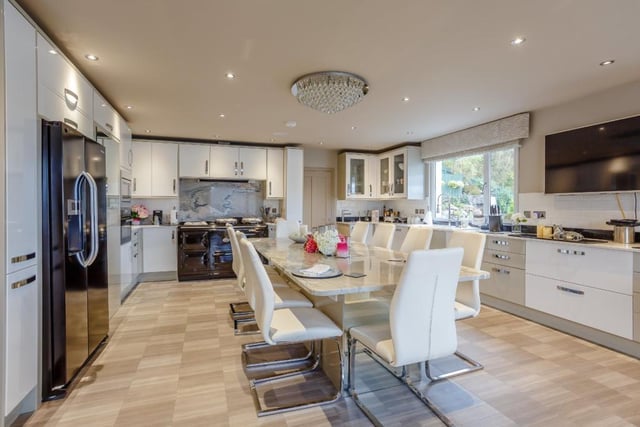 The kitchen provides a range of contemporary units including a large granite central island/dining table, walk-in larder, quartz worktops, breakfast bar, four-oven Aga, and modern integrated appliances including a wine chiller.