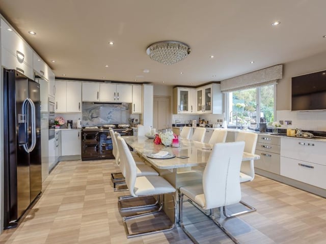 The kitchen provides a range of contemporary units including a large granite central island/dining table, walk-in larder, quartz worktops, breakfast bar, four-oven Aga, and modern integrated appliances including a wine chiller.