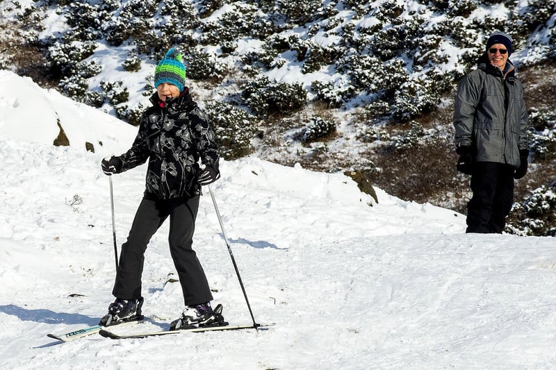 A woman skis down the side of Arthur's Seat while a snowboarder waits his turn.