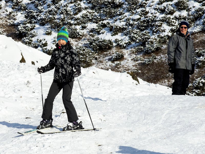 A woman skis down the side of Arthur's Seat while a snowboarder waits his turn.