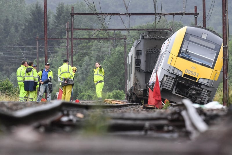 Rail workers stand near a derailed carriage belonging to the Belgium SNCB train service, the day after heavy rains and floods near the town of Rochefort on July 16, 2021. -