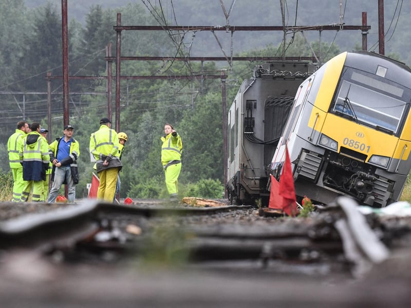 Rail workers stand near a derailed carriage belonging to the Belgium SNCB train service, the day after heavy rains and floods near the town of Rochefort on July 16, 2021. -