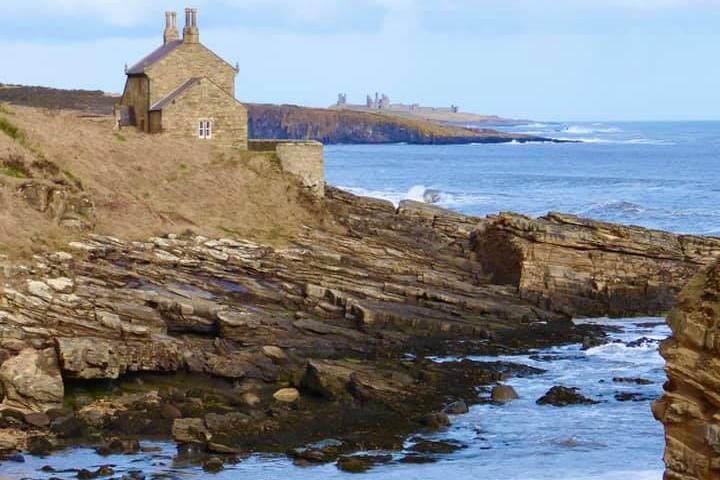 Howick bathing house, with Dunstanburgh Castle further along the coast.