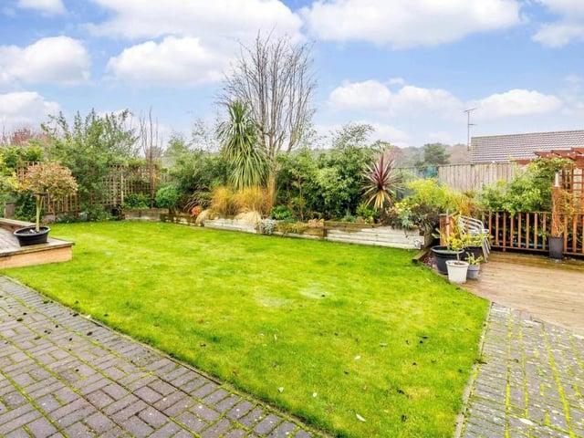 The enclosed rear garden features a central lawn, block-paved and decked patios beneath a triangular-shaped pergola, and raised flowerbeds with ample plants and shrubs offering good screening from neighbouring properties.