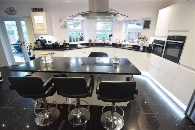 Let's move in to the modern kitchen now. It is an open-plan room with a central island breakfast bar and a range of modern white gloss wall and base units with black worktops. There is also an inset sink basin with a drainer and mixer tap.