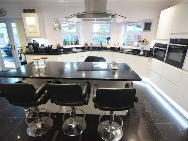 Let's move in to the modern kitchen now. It is an open-plan room with a central island breakfast bar and a range of modern white gloss wall and base units with black worktops. There is also an inset sink basin with a drainer and mixer tap.
