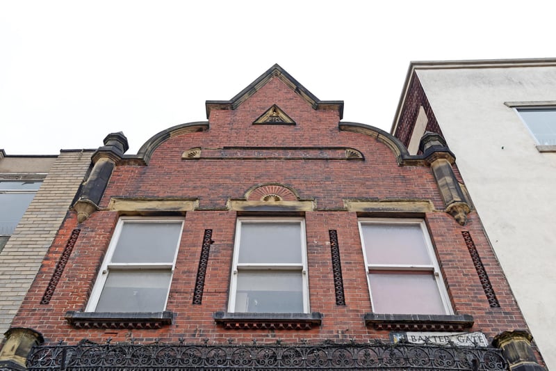 A narrow Victorian building with ornate gable and decorative stone and ironwork. It was Leesing's noted Prk Butchers, from 1894 until 1980, as the name and date above the first floor indicate.