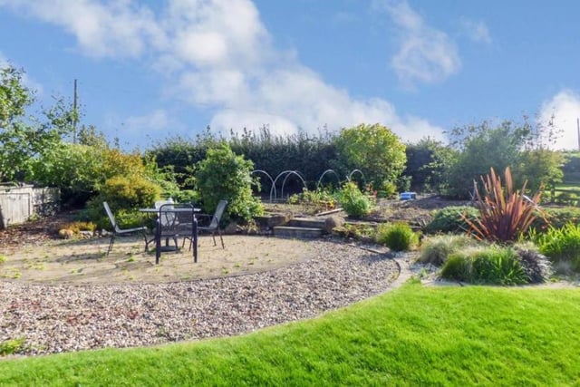 At the end of the garden is a circular paved patio area and vegetable patch with raised planting areas and mature fruit trees.