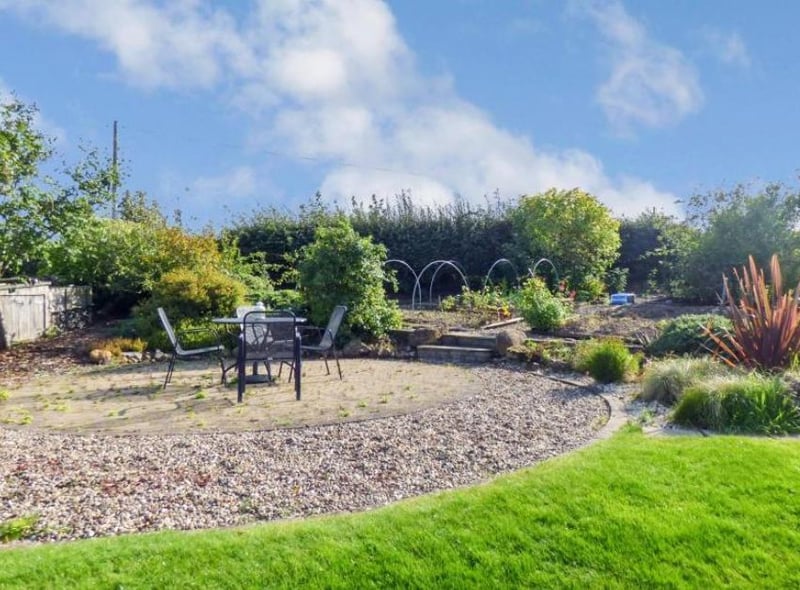 At the end of the garden is a circular paved patio area and vegetable patch with raised planting areas and mature fruit trees.