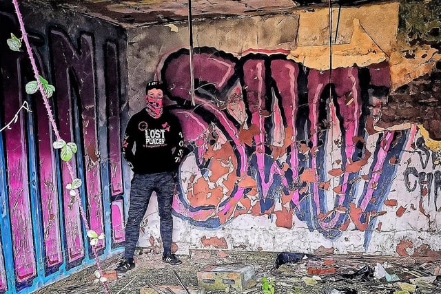 Urban explorer Lost Places & Forgotten Faces next to some graffiti inside the complex.