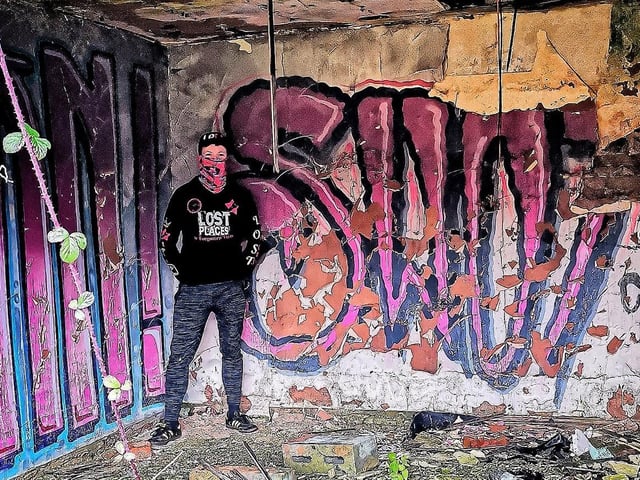 Urban explorer Lost Places & Forgotten Faces next to some graffiti inside the complex.