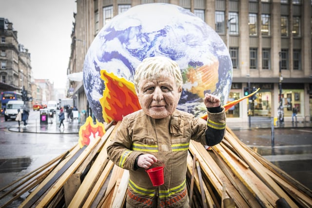 Campaigner wearing a 'big heads' of Boris Johnson takes part in Oxfam's 'Ineffective Fire-Fighting World Leaders' protest performance in front of a 10 foot globe with a simulated bonfire, during the official final day of the Cop26 summit in Glasgow. Picture date: Friday November 12, 2021.