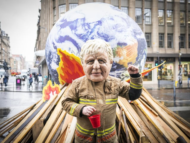 Campaigner wearing a 'big heads' of Boris Johnson takes part in Oxfam's 'Ineffective Fire-Fighting World Leaders' protest performance in front of a 10 foot globe with a simulated bonfire, during the official final day of the Cop26 summit in Glasgow. Picture date: Friday November 12, 2021.