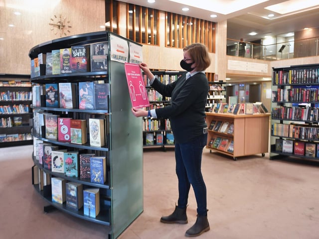 Priciple librarian, Dawn Vallance with sign encouraging social distancing.