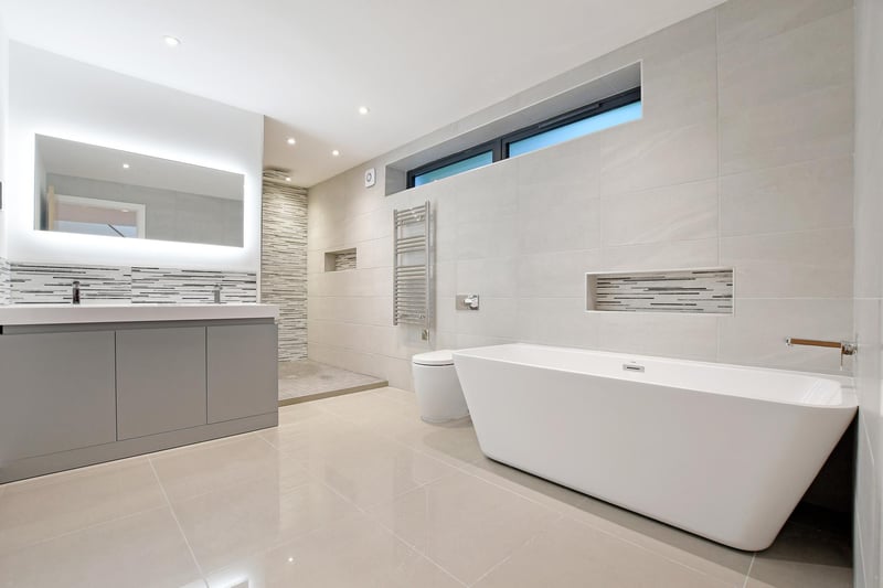 There’s a suite in white, which comprises of a low-level WC and two wash hand basins, storage beneath and an illuminated vanity mirror above. To one corner, there’s a Mode bath with a Mode chrome mixer tap. Also, there’s a wet room style shower area with a fitted rain head shower.