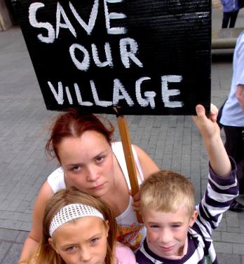 Protesters outside the mansion house with a sign that says 'Save Our Village.'
