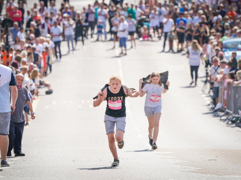 Competitors in the Junior Race take part in the Scottish Coal Carrying Championships through the streets of Kelty in Fife. Picture date: Saturday August 28, 2021. PA Photo. The annual event is one of only two Coal Races in the world and the men's race requires participants to carry a 50-kilo bag of coal and the women's race requires a 25-kilo bag of coal to be carried over 1000 metres through the village. Photo credit should read: Jane Barlow/PA Wire