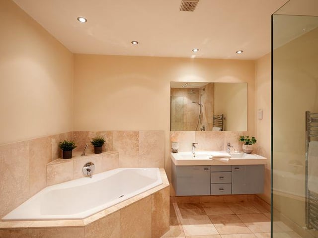 There are five bathrooms throughout the property, including this modern suite complete with dual sinks, a walk in shower, and spacious corner bath.