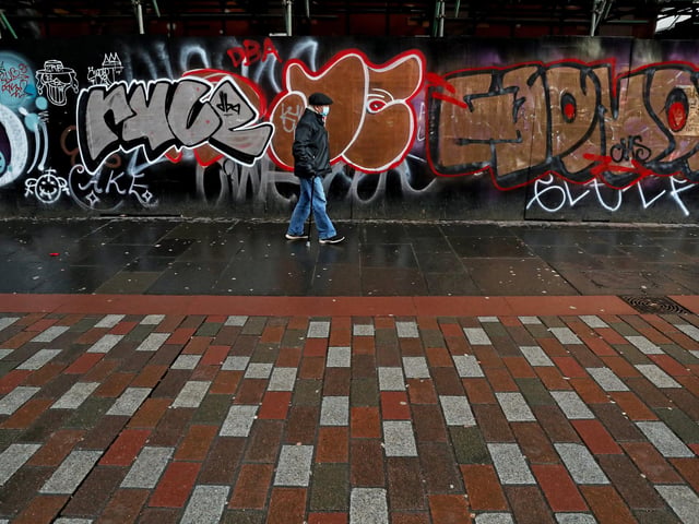 A man wearing a face mask walks past graffiti on Argyle Street in Glasgow city centre