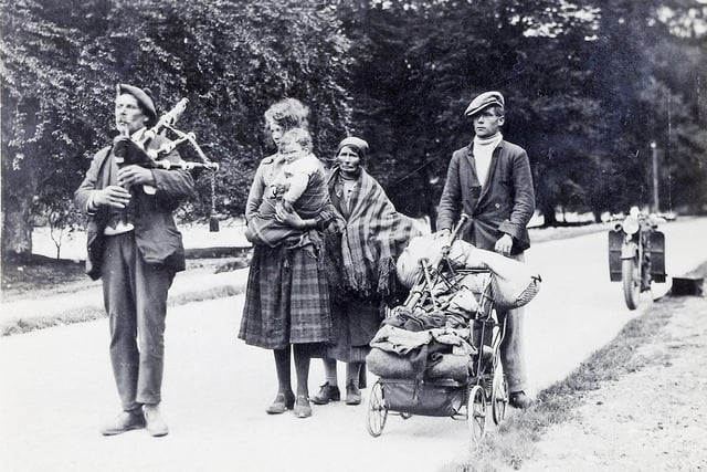 A piper escorts a travelling family, with some of their possessions - including a set of pipes - wheeled along in the pram.