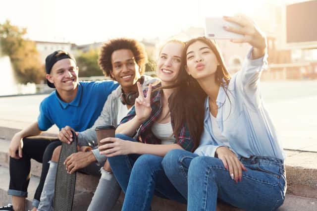 Group of multiethnic teenagers taking selfie, sitting on stairs outdoor, summer evening, sun flare