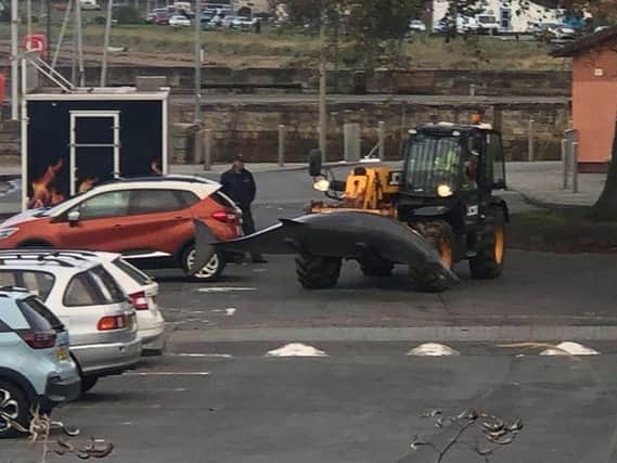 The dead whale is carried through the car park on a forklift truck.