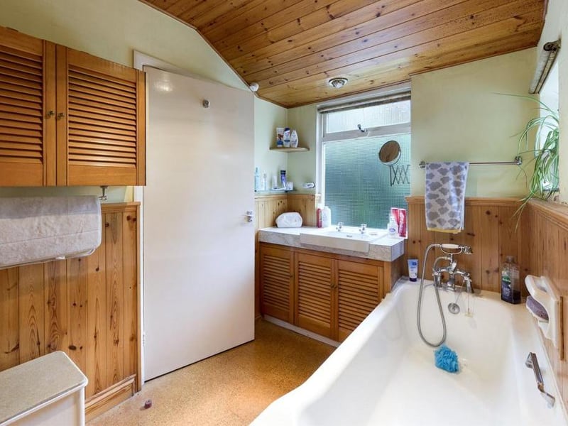 Bathroom - Low level WC, pedestal wash basin and panelled bath with shower head mixer tap; single glazed timber framed window and electric radiator panel.