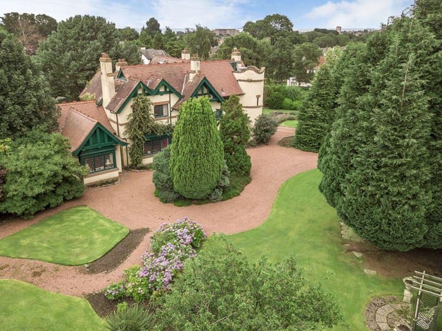 The drive leads to the magnificent house with its turret, framed by stone mullions and an ornate balcony