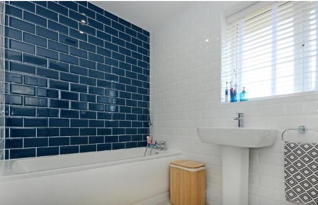 The bathroom, complete with bath next to a blue tiled wall