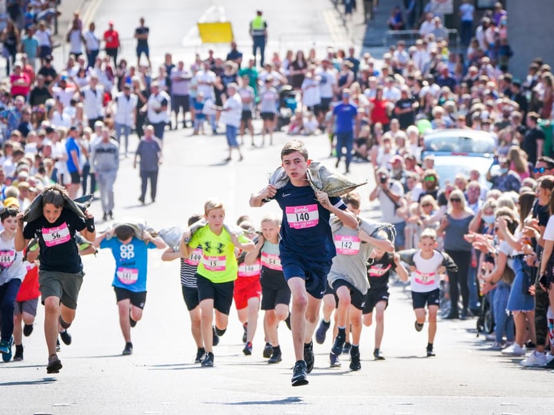 Competitors in the Junior Race take part in the Scottish Coal Carrying Championships through the streets of Kelty in Fife. Picture date: Saturday August 28, 2021. PA Photo. The annual event is one of only two Coal Races in the world and the men's race requires participants to carry a 50-kilo bag of coal and the women's race requires a 25-kilo bag of coal to be carried over 1000 metres through the village. Photo credit should read: Jane Barlow/PA Wire