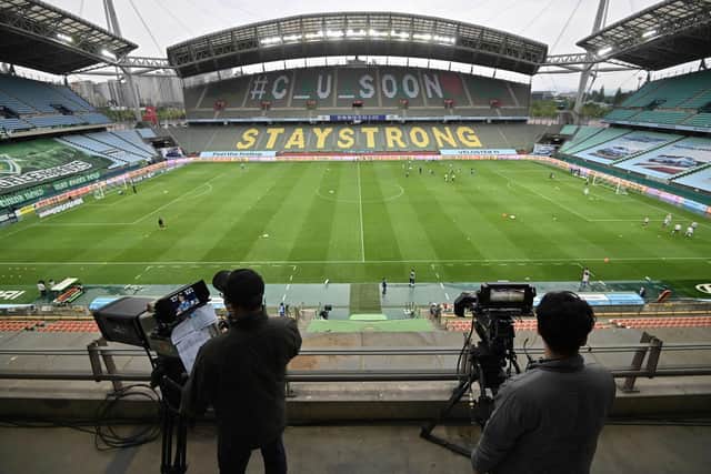 TOPSHOT - Cameramen take footages while football players warm up on the ground prior to the opening game of South Korea's K-League football match between Jeonbuk Hyundai Motors and Suwon Samsung Bluewings at Jeonju World Cup Stadium in Jeonju on May 8, 2020. - The towering stands of the 42,477-capacity Jeonju World Cup Stadium stood empty on May 8 and would remain that way as football restarted in South Korea after the coronavirus behind closed doors, but with unprecedented international TV audiences:  JUNG YEON-JE/AFP via Getty Images